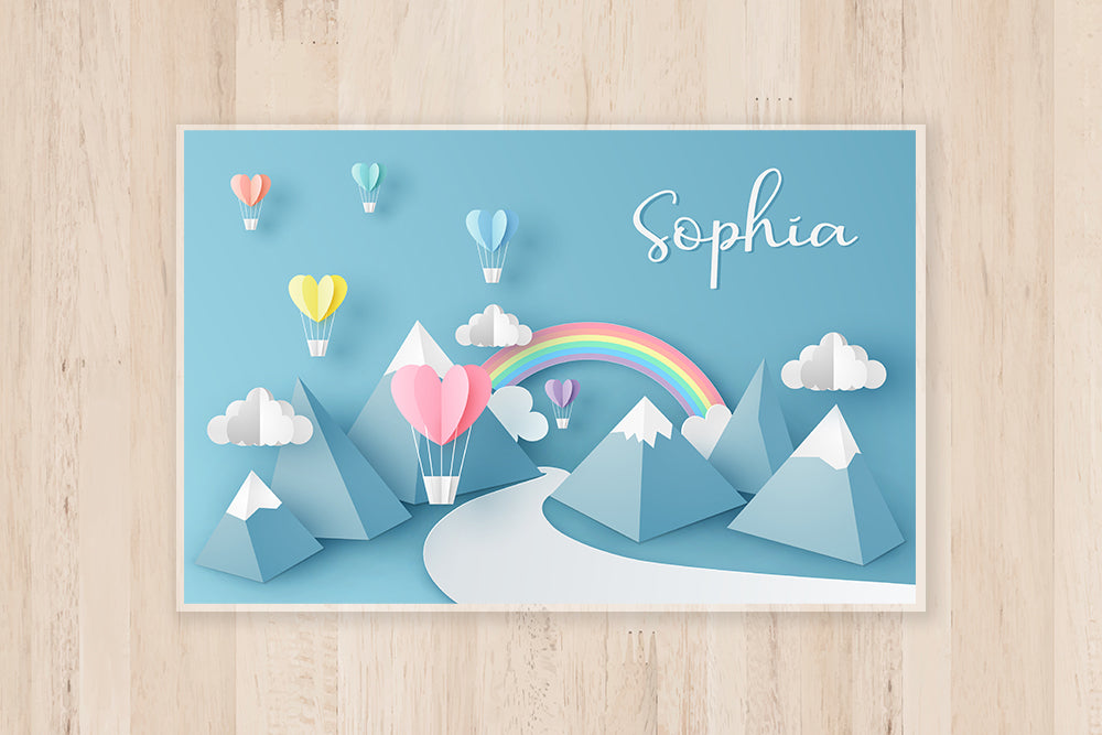 Placemat for kids with a Rainbow Design in the center, Mountains and Air Balloons in the background. Personalized child's name on the top right corner